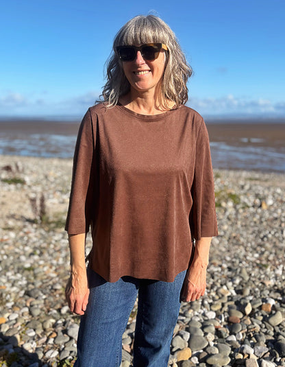 woman wearing vegan suede brown boxy t shirt with 3/4 length sleeves with jeans on a beach