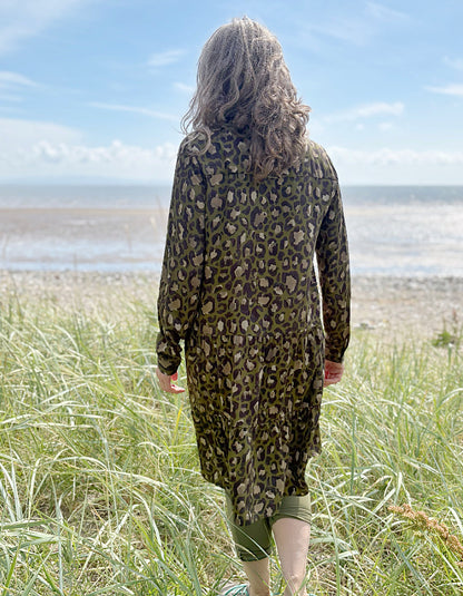 Person wearing a leopard print dress standing on a grassy field with a beach and blue sky in the background