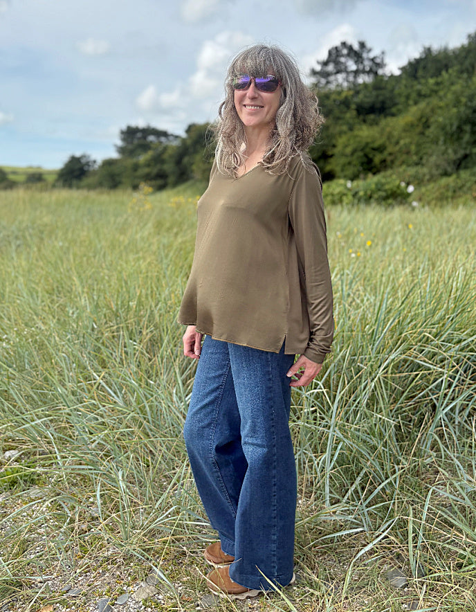 Woman standing in a field wearing an olive green top and blue jeans.