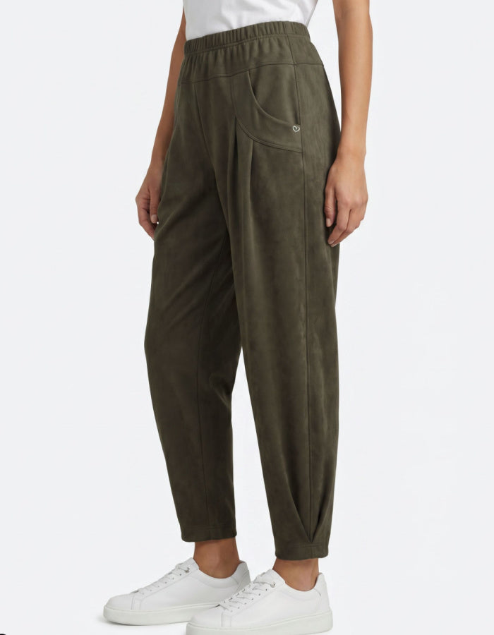A person wearing olive green jogger-style pants with an elastic waistband, side pockets, and a relaxed tapered fit, paired with white sneakers against a light gray studio background.