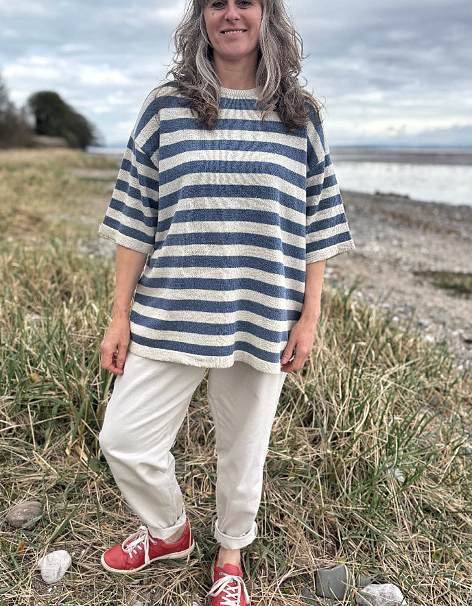 Woman wearing a Breton striped organic cotton sweater and white pants standing in a field with a beach in the background.