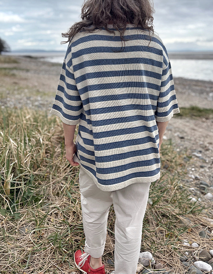 Woman wearing a Breton striped organic cotton sweater and white pants standing in a field with a beach in the background.