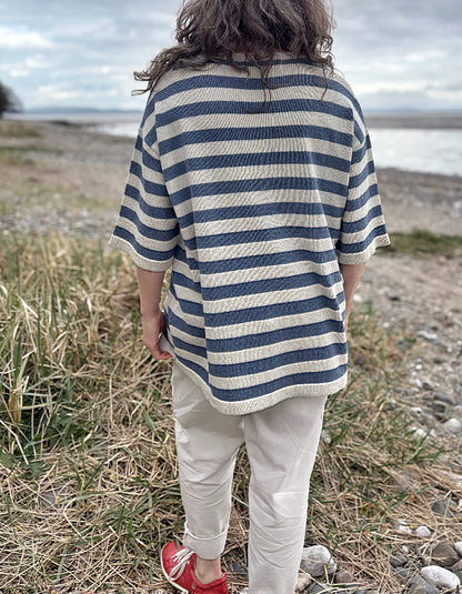 Woman wearing a Breton striped organic cotton sweater and white pants standing in a field with a beach in the background.