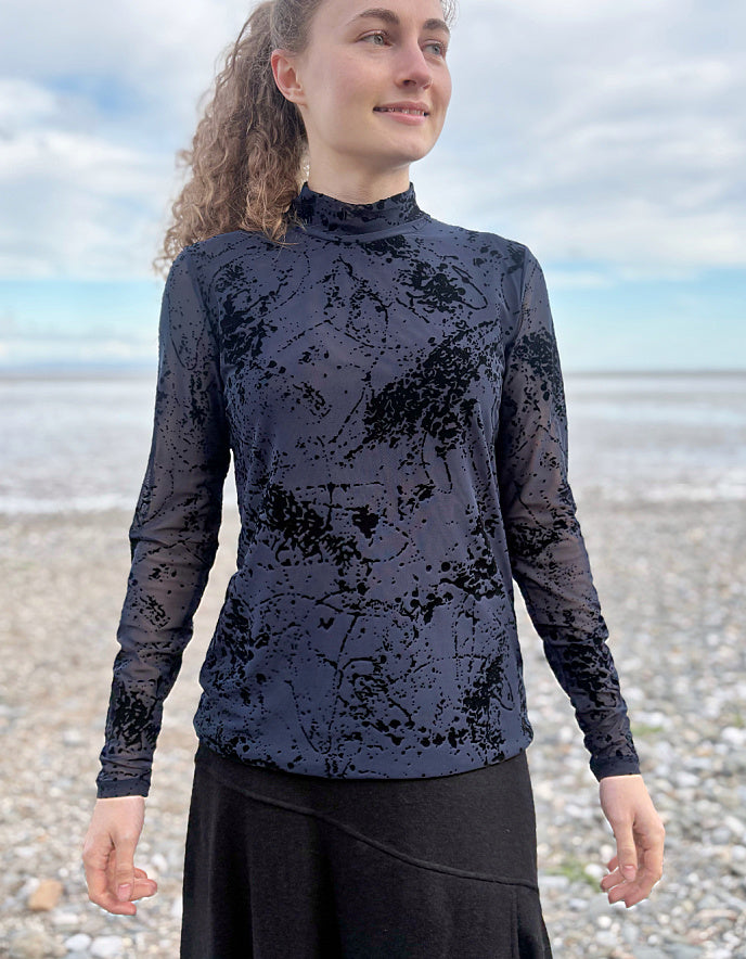 lady wearing tight fit navy mesh top with velvet splatter overlay print with a black skirt on a beach