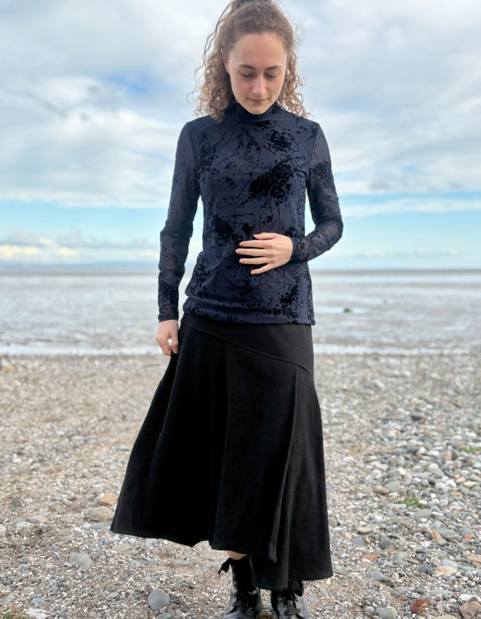 lady wearing tight fit navy mesh top with velvet splatter overlay print with a black skirt on a beach