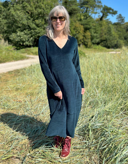 Woman in a long dark teal velvet dress standing in a field with trees in the background