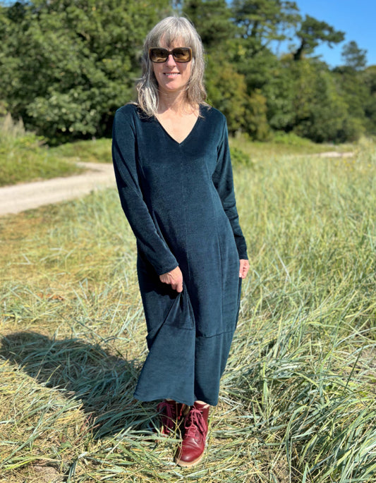 Woman in a long dark teal velvet dress standing in a field with trees in the background