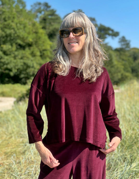 Woman wearing a burgundy outfit standing in a field with trees in the background