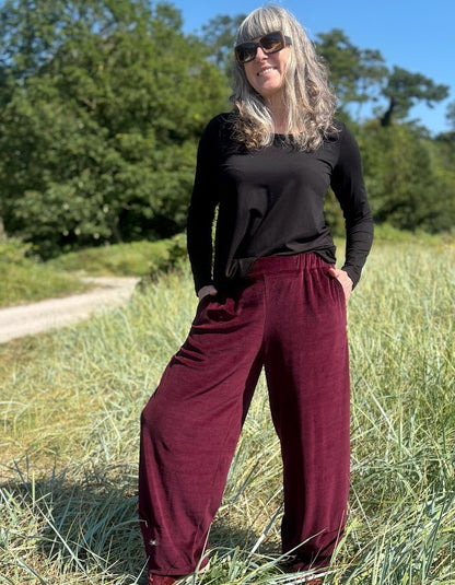 Woman wearing a black top and burgundy velvet pants standing in a grassy field.