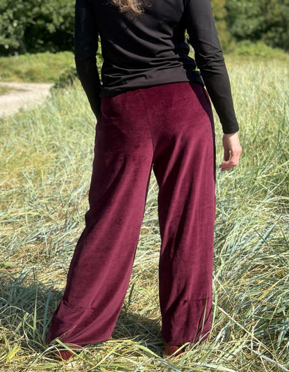 Woman wearing a black top and burgundy velvet pants standing in a grassy field.