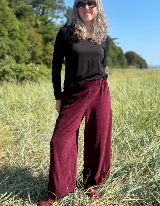 Woman wearing a black top and burgundy velvet pants standing in a grassy field.