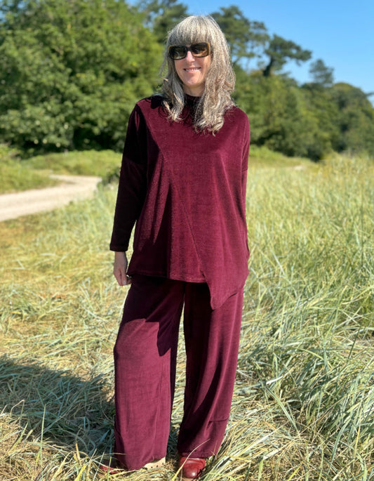 Woman in a burgundy velvet co-ord trouser and top outfit standing in a field with trees in the background