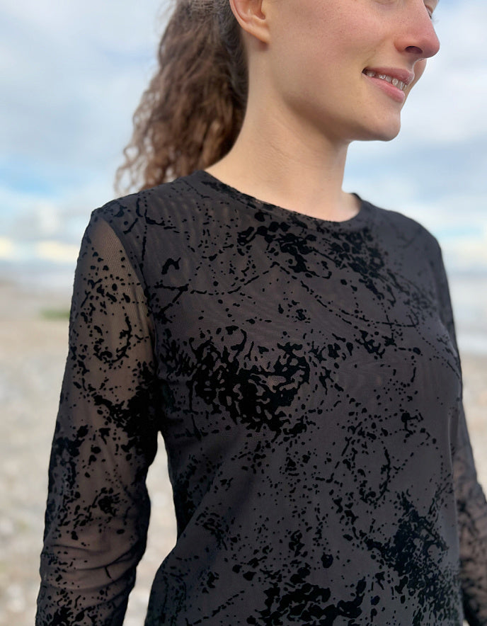Person wearing a black lace long-sleeve top with a blurred background
