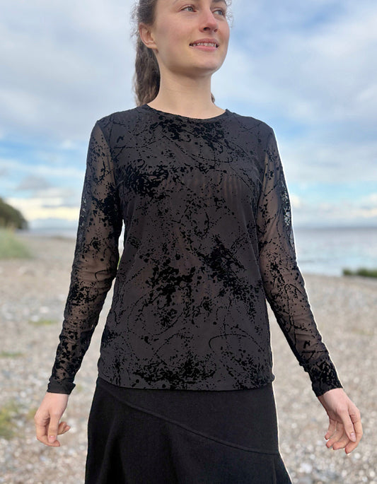 Person wearing a black long-sleeve top with sheer overlay on a beach
