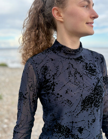 lady wearing tight fit navy mesh top with velvet splatter overlay print with a black skirt on a beach