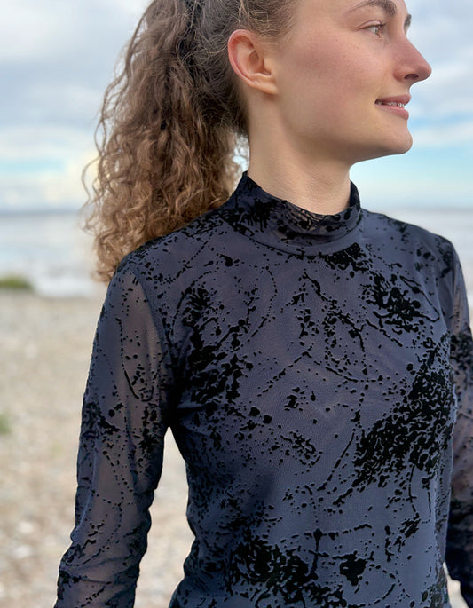 lady wearing tight fit navy mesh top with velvet splatter overlay print with a black skirt on a beach