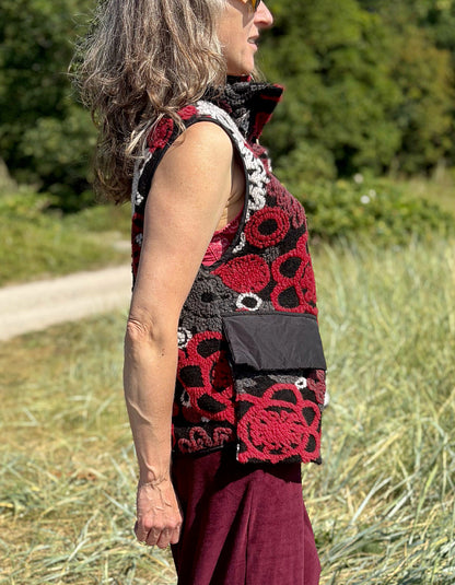 Woman wearing a floral patterned vest and burgundy pants standing in a field.