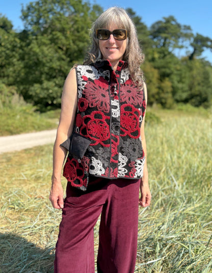 Woman wearing a floral patterned vest and burgundy pants standing in a field.