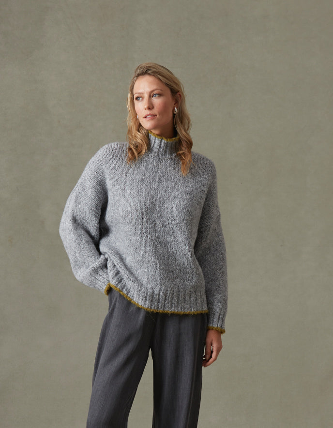 Woman wearing a gray knitted sweater and pants against a beige background