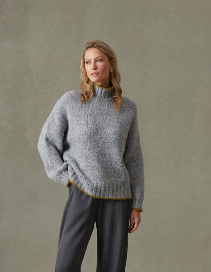 Woman wearing a gray knitted sweater and pants against a beige background
