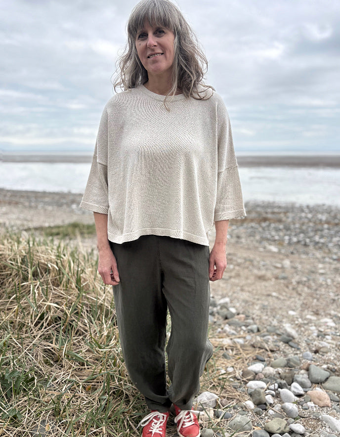 Woman standing outdoors in a natural setting wearing a cream organic cotton sweater and dark green tercel pants.