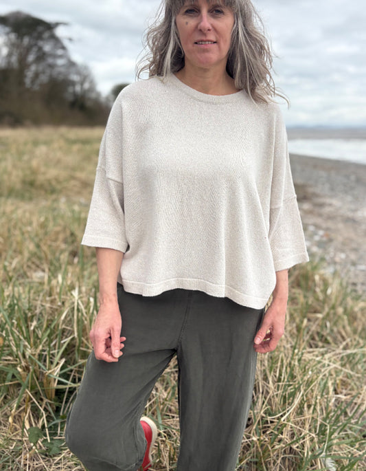 Woman standing outdoors in a natural setting wearing a cream organic cotton sweater and dark green tercel pants.