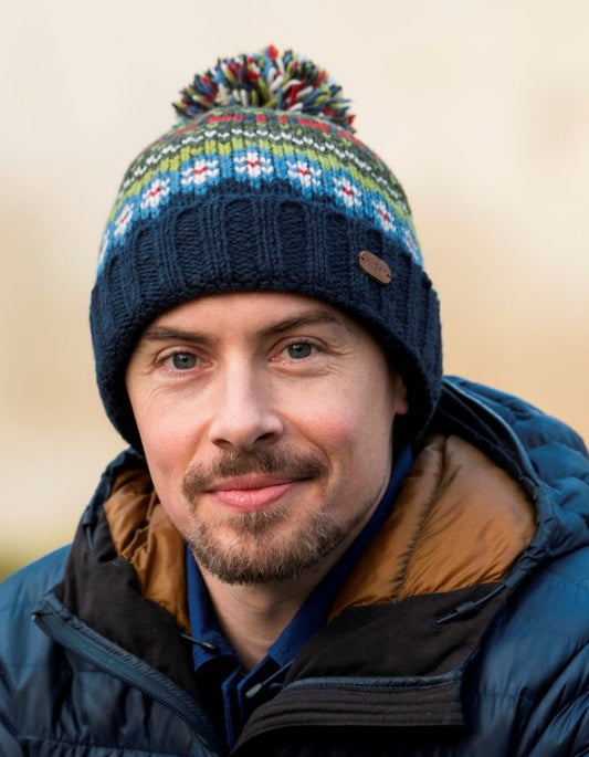 Man wearing a colorful knitted hat and blue jacket with a beige background