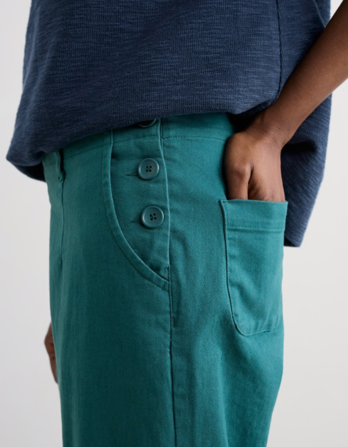 Teal pants with buttons worn by a person on a plain background