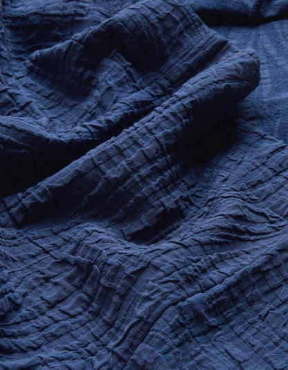 A close-up of dark navy blue crinkled gauze fabric, showing its textured weave and soft folds.