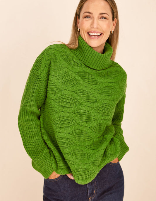 Woman wearing a green cable knit sweater against a beige background