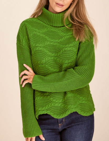 Green cable knit sweater worn by a person on a beige background