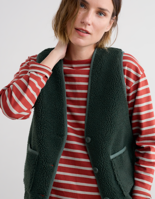 Woman wearing a red and white striped shirt with a green fleece vest on a plain background