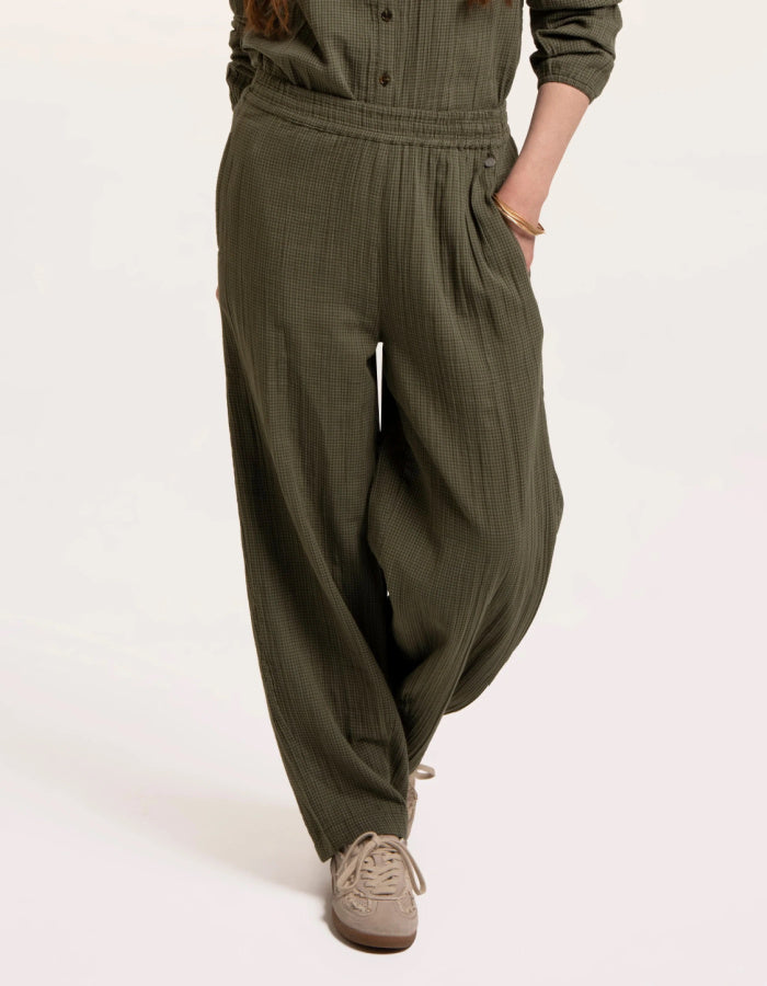 A person wearing loose, wide-leg olive green pants with a matching top and beige sneakers, photographed against a plain light background.