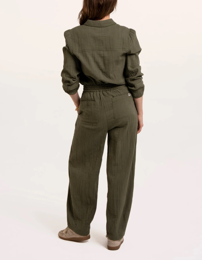 A woman modelling an olive green checked barrel leg trousers paired with beige sneakers, against a plain white studio background.