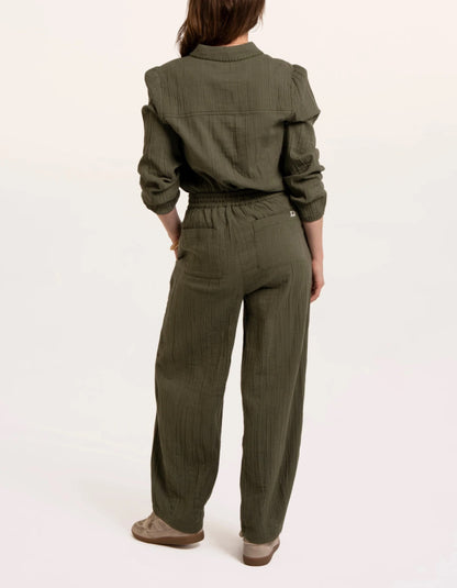 A woman modelling an olive green checked barrel leg trousers paired with beige sneakers, against a plain white studio background.
