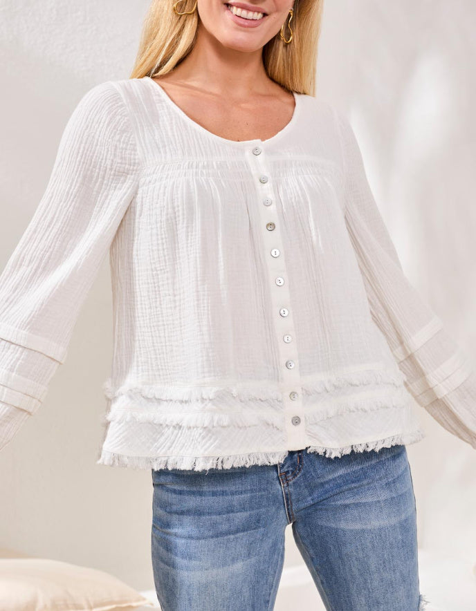 Woman wearing a white blouse with long sleeves and blue jeans against a neutral background