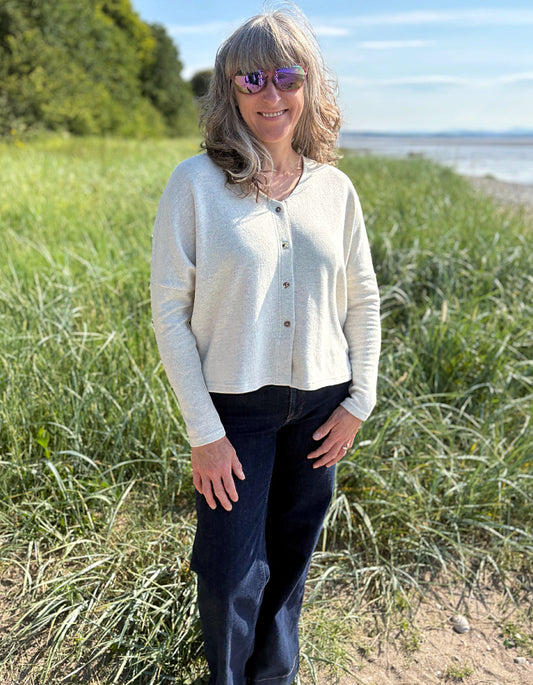 Woman standing in a grassy field with a scenic background wearing a winter white fleece cardigan