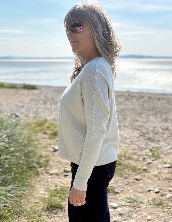 Woman standing in a grassy field with a scenic background wearing a winter white fleece cardigan