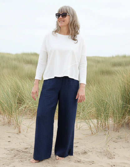 Woman wearing a white top and sunglasses on a sandy beach with grasses.