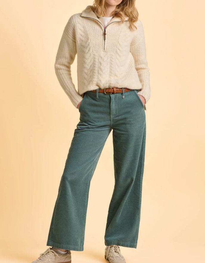 Person wearing a cream sweater and teal pants on a beige background