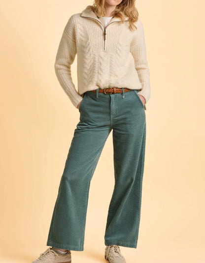 Person wearing a cream sweater and teal pants on a beige background
