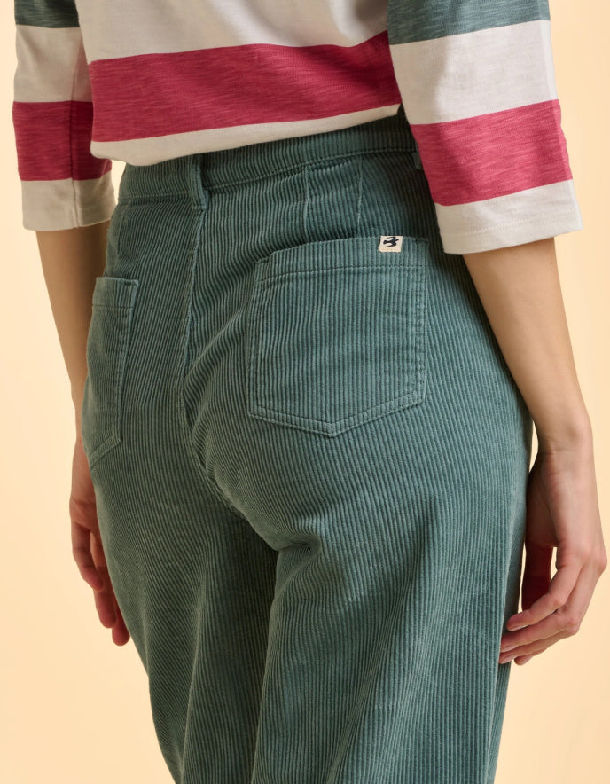 Green corduroy pants worn with a striped shirt on a beige background