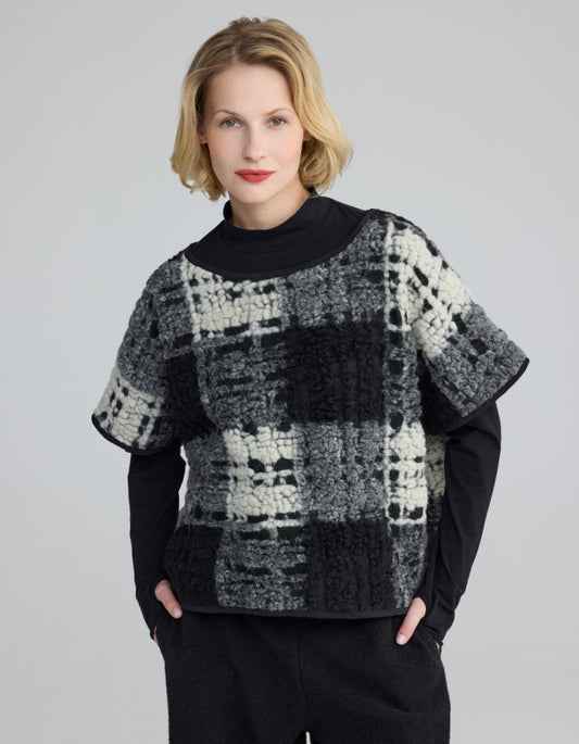 Woman wearing a black and white patterned sweater over a black turtleneck on a gray background