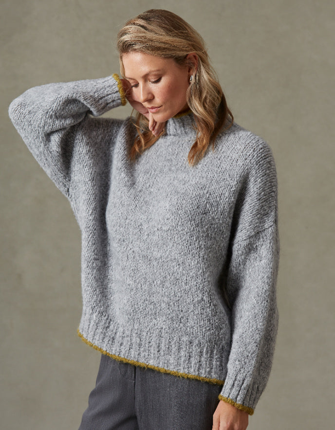 Woman wearing a gray knitted sweater with yellow trim against a neutral background