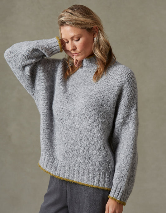 Woman wearing a gray knitted sweater with yellow trim against a neutral background