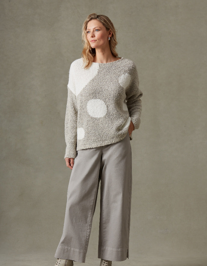 Woman wearing a patterned sweater and pants against a plain background