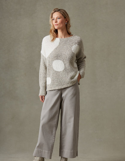 Woman wearing a patterned sweater and pants against a plain background