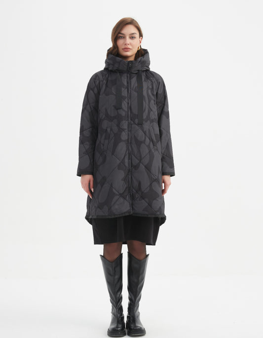 Woman wearing a long dark coat with a pattern on a white background